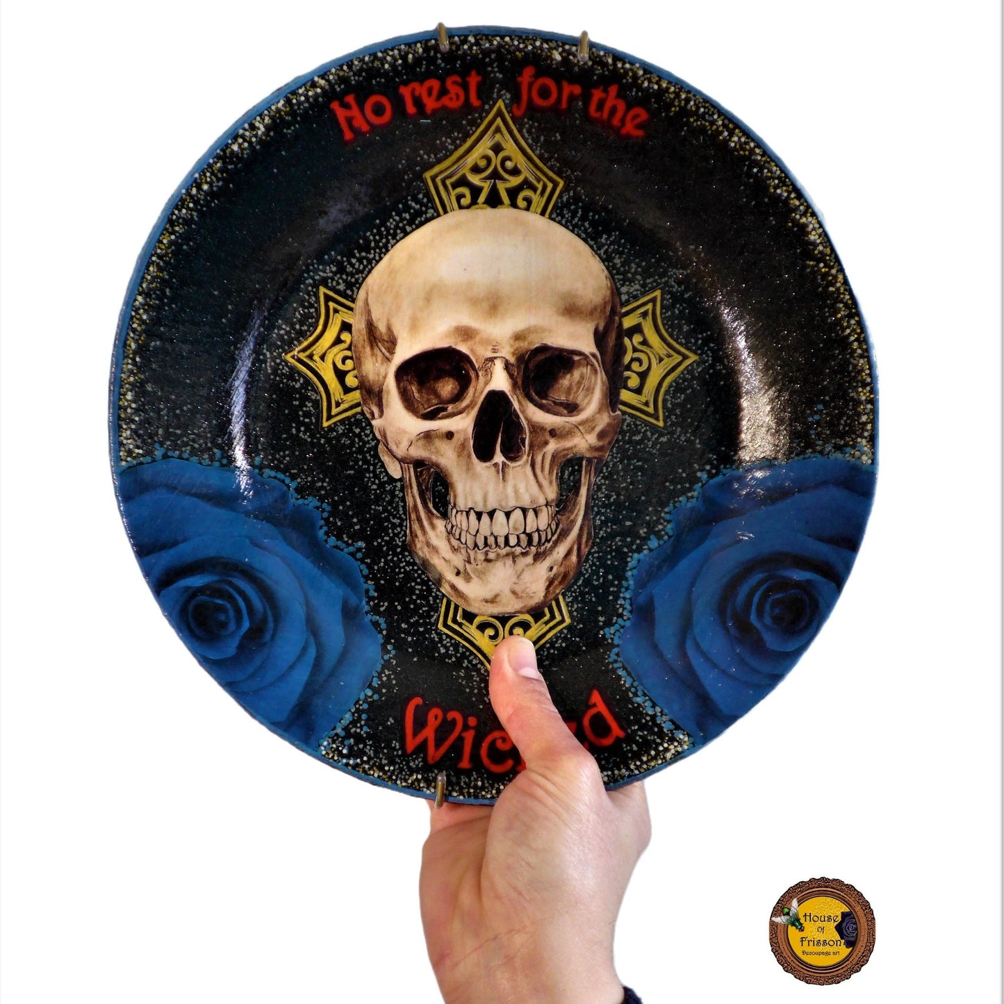 House of Frisson "No Rest For The Wicked" Black Wall Plate front. Collage artwork featuring a skull, a cross, and blue roses, on a black background. Holding the plate.