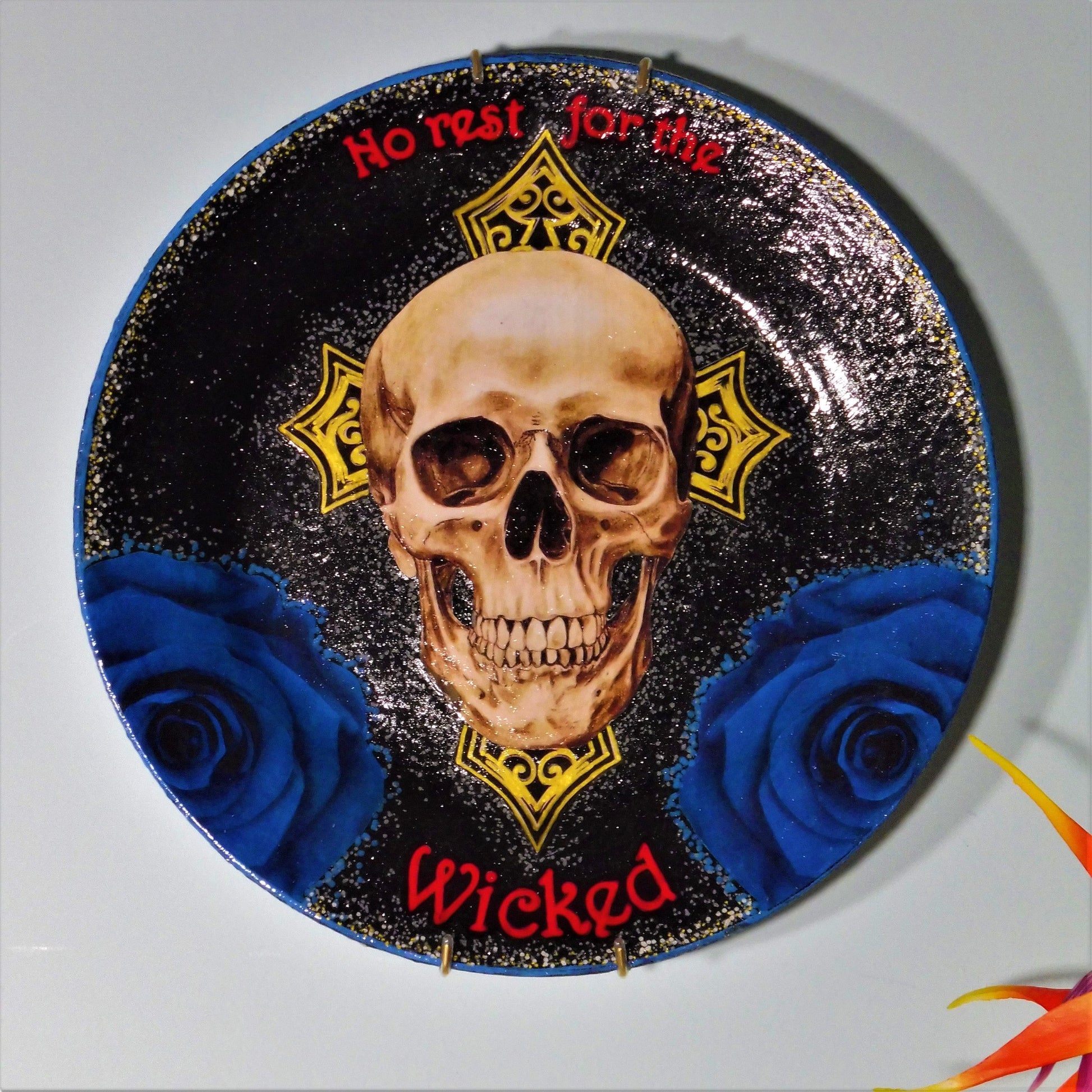 House of Frisson "No Rest For The Wicked" Black Wall Plate front. Collage artwork featuring a skull, a cross, and blue roses, on a black background. Plate hanging on a wall.